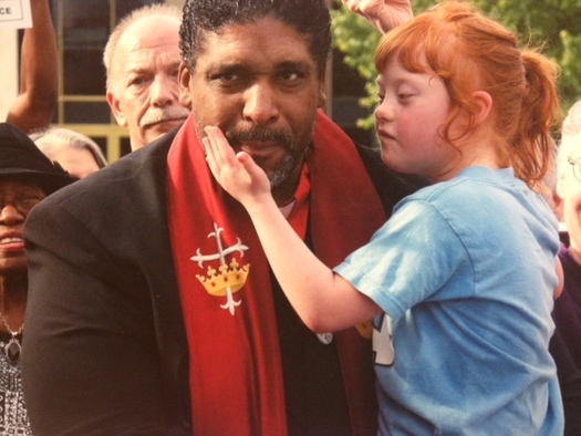 A picture of Rev. Dr. William J. Barber II holding a child in his arms.